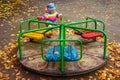 Child is riding carousel in children`s playground in autumn. Little girl playing.