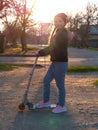 Child riding on kickscooter alone. Blonde cute girl on scooter on spring city park street background. Active lifestyle