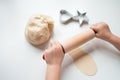Child rolling dough with rolling pin and cookie cutter on white surface Royalty Free Stock Photo