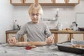 Child with rolling pin in his hands rolls out the cookie dough