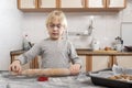 Child with rolling pin in his hands rolls out the cookie dough. Cooking with children