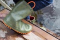 Child in rubber boots stands on wooden flooded bridge and puts his legs in water of river