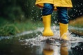 Child in rubber boots and yellow raincoat jumping in puddle