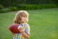 Child with rugby ball. Kid boy having fun and playing american football on green grass park. Royalty Free Stock Photo