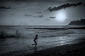 A child running along the seashore against the backdrop of storm waves and the setting sun