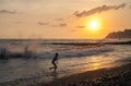 A child running along the seashore against the backdrop of storm waves and the setting sun