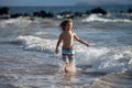 Child running through water close to shore along the sea beach. A boy runs along the sea coast. Rest of children on Royalty Free Stock Photo