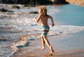 Child running through water close to shore along the sea beach. A boy runs along the sea coast. Rest of children on Royalty Free Stock Photo