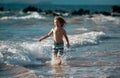 Child running through water close to shore along the sea beach. A boy runs along the sea coast. Rest of children on Royalty Free Stock Photo