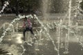 A child runs among the jets of water in the town square. Splashes of the fountain in the summer