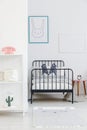 Child`s bed with black metal frame in a small, simple bedroom in