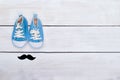 Child`s blue sneakers and mustaches lie on a white wooden backgr Royalty Free Stock Photo