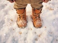 a child\'s feet in light brown winter boots on the snow