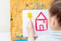 Child is drawing yellow sun with red house Royalty Free Stock Photo