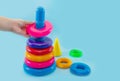 Child`s hand folds multi-colored pyramid isolated on blue background.Close-up of a child`s hand playing with a toy pyramid.