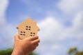 Child`s hand holding small wooden toy house with blue sky and white clouds background. Royalty Free Stock Photo