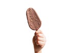 A child's hand holds a chocolate ice cream on a stick, a popsicle with nuts, isolated on a white background Royalty Free Stock Photo