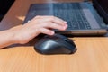 A child`s hand holds a computer mouse next to a laptop keyboard on a wooden table Royalty Free Stock Photo