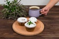 A child`s hand holds a cup of tea and mint near the board with muffins with black currant, on a background of flowers