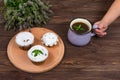 A child`s hand holds a cup of tea and mint near the board with muffins with black currant, on a background of flowers