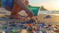 A child& x27;s hand picking up microplastics from the sand, with a bucket and shovel in the background, representing the