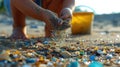 A child& x27;s hand picking up microplastics from the sand, with a bucket and shovel in the background, representing the