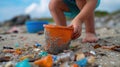 A child& x27;s hand picking up microplastics from the sand, with a bucket and shovel in the background, representing the