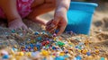 A child& x27;s hand picking up microplastics from the sand, with a bucket and shovel in the background, representing the