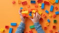 A child\'s hand playing with Lego. There are Legos scattered on the table with a orange background