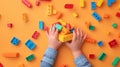 A child\'s hand playing with Lego. There are Legos scattered on the table with a orange background