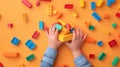 A child\'s hand playing with Lego. There are Legos scattered on the table with a orange background