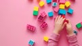 A child\'s hand playing with Lego. There are Legos scattered on the table with a pink background