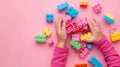 A child\'s hand playing with Lego. There are Legos scattered on the table with a pink background