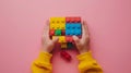 A child\'s hand playing with Lego. There are Legos scattered on the table with a pink background