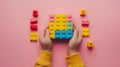 A child\'s hand playing with Lego. There are Legos scattered on the table with a pink background