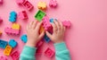 A child\'s hand playing with Lego. There are Legos scattered on the table with a pink background