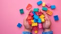 A child\'s hand playing with Lego. There are Legos scattered on the table with a pink background