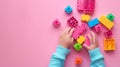 A child\'s hand playing with Lego. There are Legos scattered on the table with a pink background