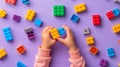 A child\'s hand playing with Lego. There are Legos scattered on the table with a purple background