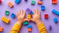 A child\'s hand playing with Lego. There are Legos scattered on the table with a purple background