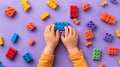 A child\'s hand playing with Lego. There are Legos scattered on the table with a purple background