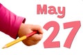 The child`s hand writes May 27 with colored pencil. White background with spring red date, business and holiday concept