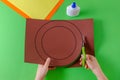 Child`s hands cut circle on brown paper with scissors, top view, on green Royalty Free Stock Photo