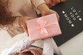 Child`s hands hold beautiful pink gift box with ribbon. Pink tulip flower and sign i love you mom in background. Top view, close- Royalty Free Stock Photo