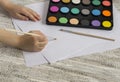 Child's hands holding a brush, paint and paper on a light wooden table. Royalty Free Stock Photo