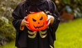 child's hands holding a bucket of pumpkin with a face in the shape of a lantern for Halloween sweets in the yard