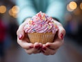 A child\'s hands holding a cupcake covered with rainbow sprinkles, joyful and bright