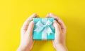 Child`s hands holding turquoise gift box on yellow background