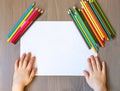 The child`s hands are painted with colored pencils on a white sheet of paper on a wooden table. the view from the top