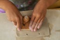 Child's hands in pottery-making process, pressing wooden tool into soft clay, creating piece of art,